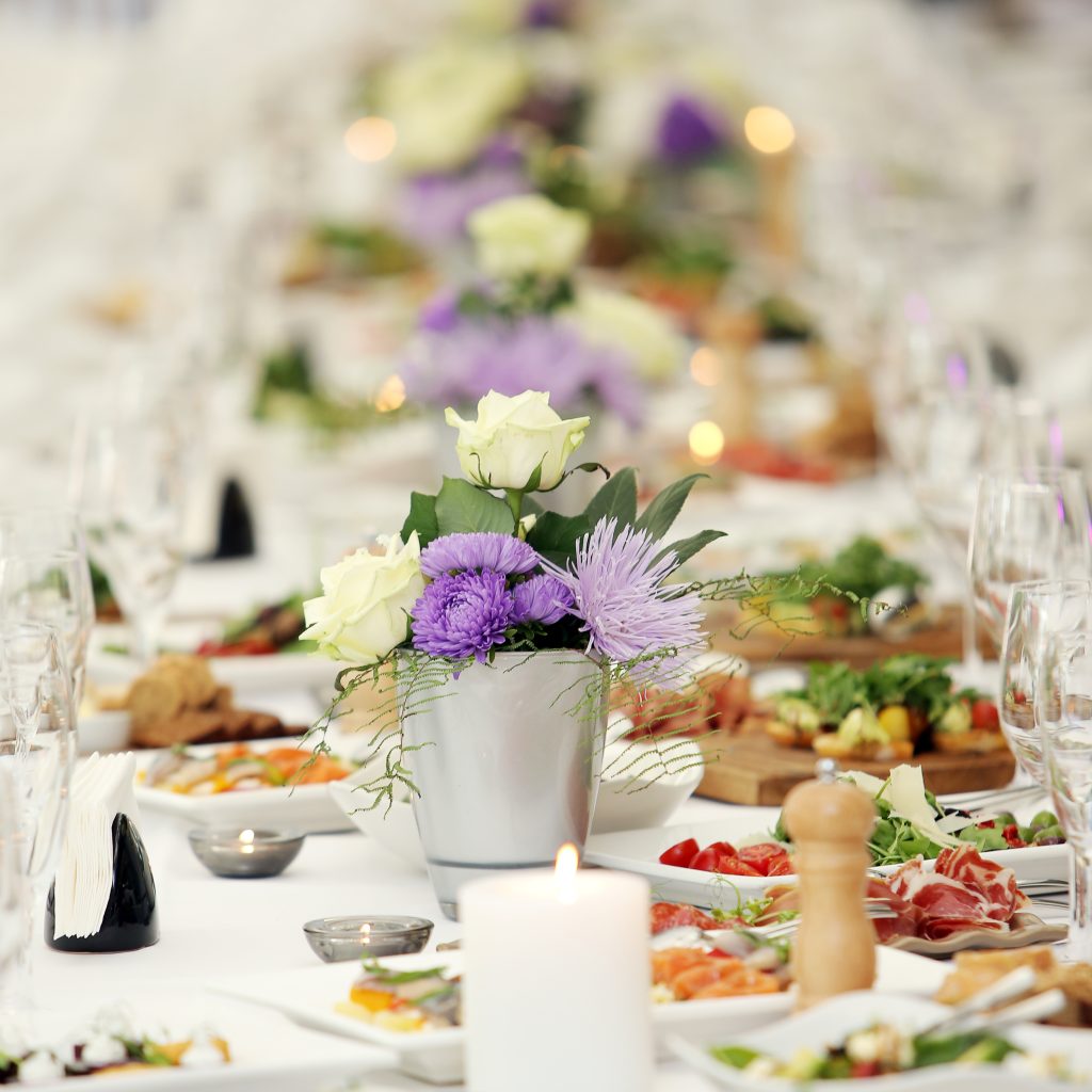 Large dining table with flowers and lots of different kinds of food at a celebration
